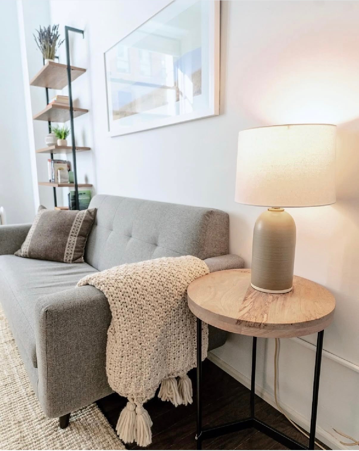 A grey couch with a textured throw and a warm lamp in Amanda Harwood's New York City therapy office